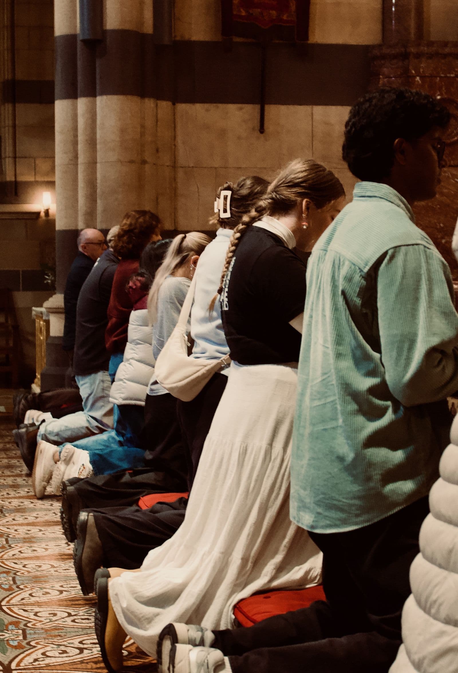 A row of people kneeling in prayer along a rail in a stone church.